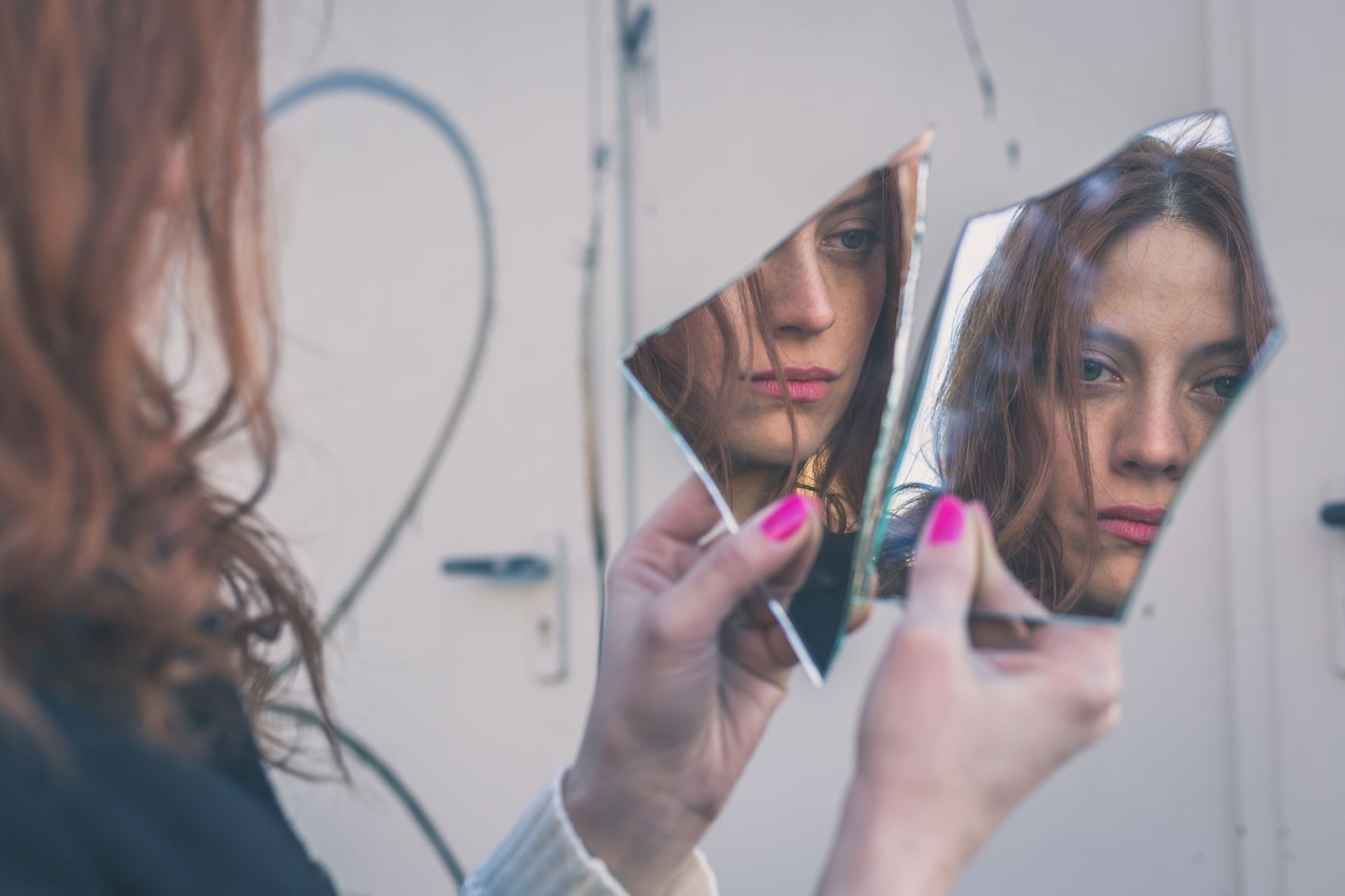 Girl looks at herself in broken mirror